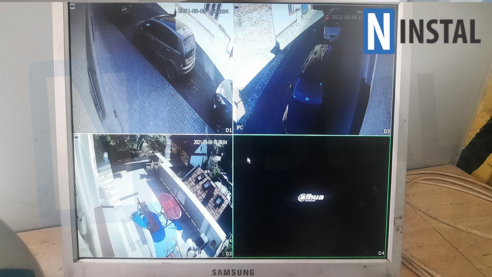 Ekran monitora Samsung wyświetlający obraz z czterech kamer monitoringu Dahua, ukazujący podjazd, ulicę i taras z meblami ogrodowymi.