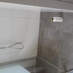 Krzysztof Mielnik Remonty i Wykończenia - Wykończona łazienka z białymi płytkami na ścianach, szarymi płytkami na podłodze, odpływem liniowym i butelką szamponu leżącą na podłodze.