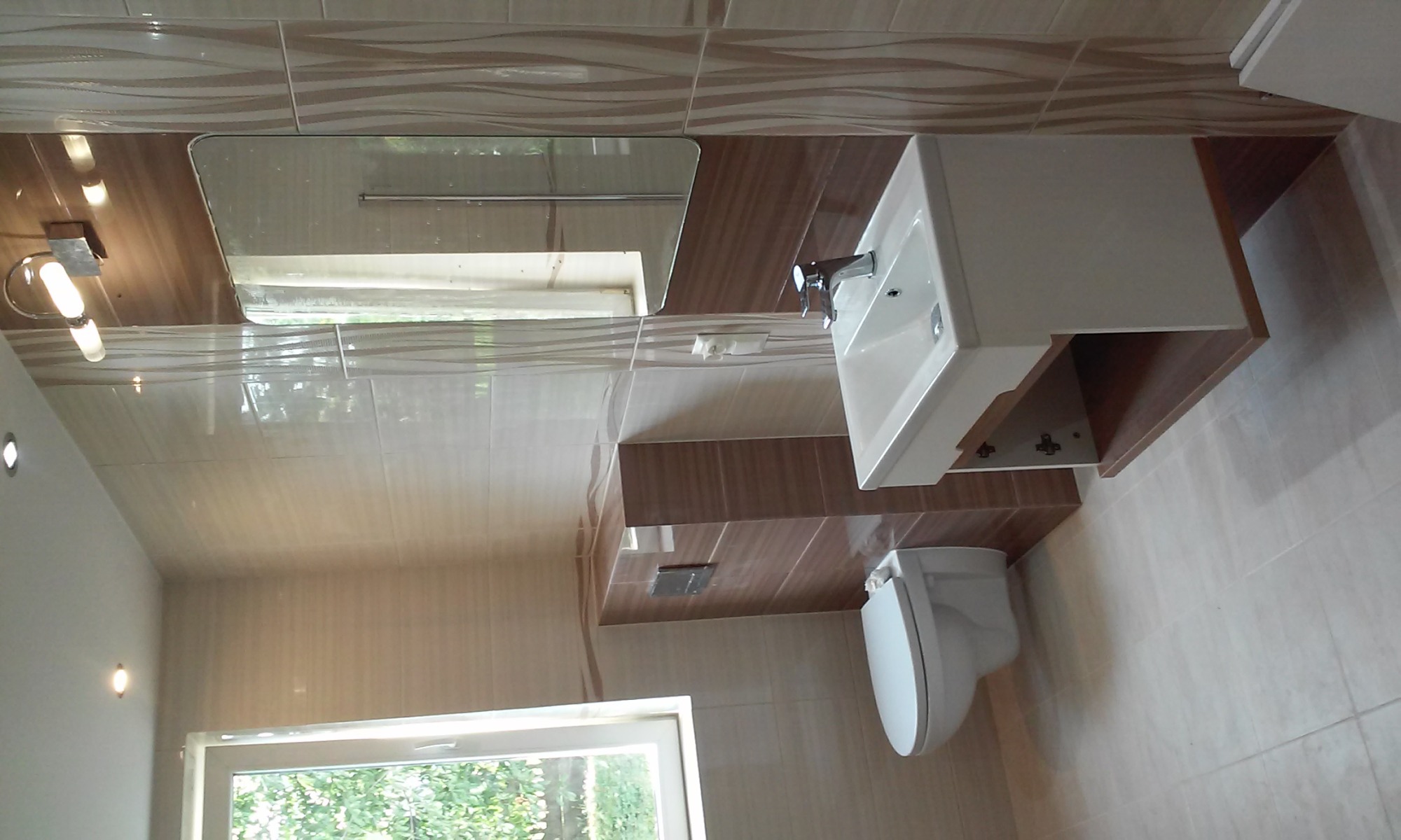 Nowoczesna łazienka w Nieledew z beżowo-brązowymi płytkami imitującymi fale, białą umywalką z szafką i lustrem.