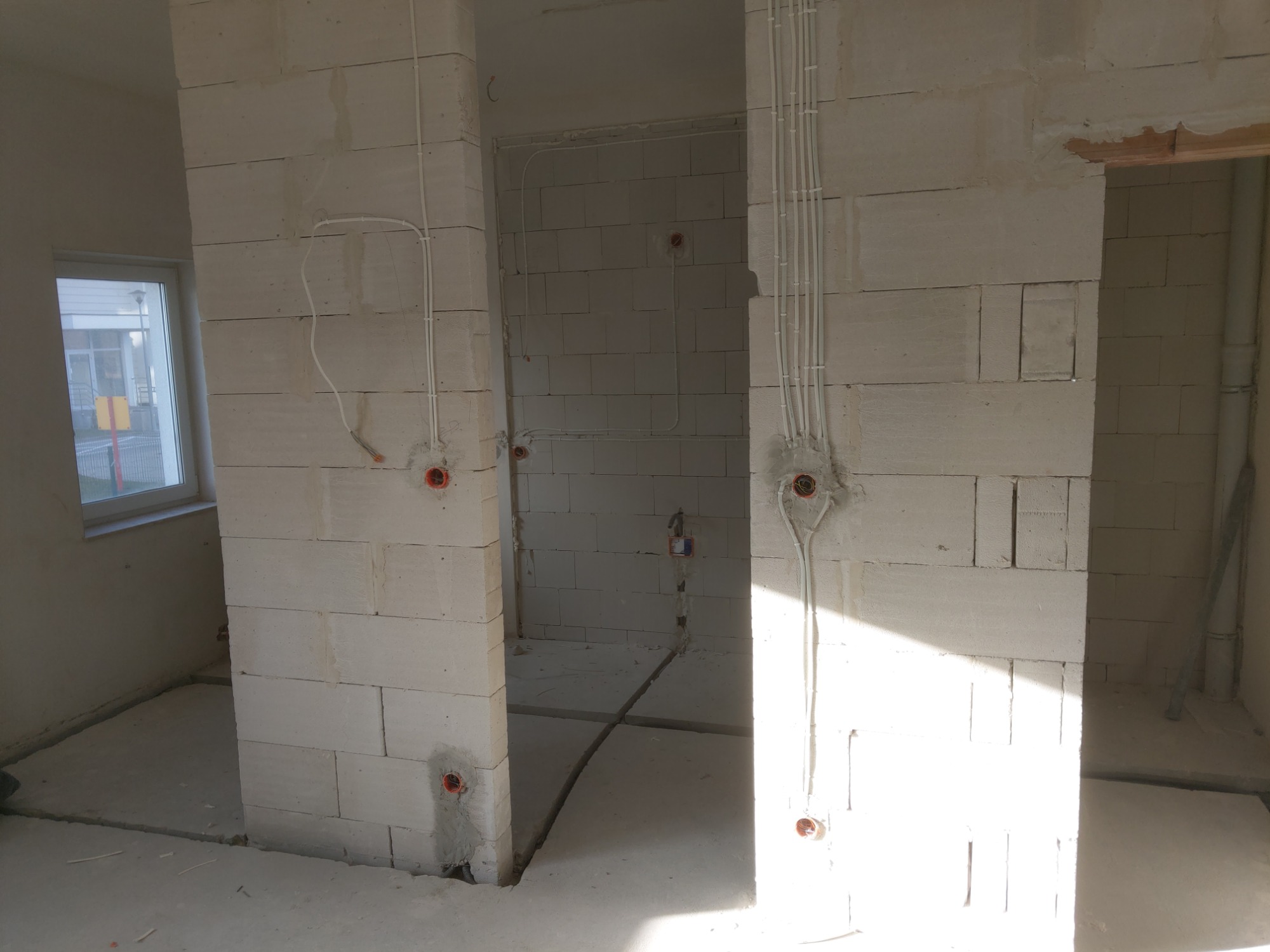 Surowy stan wnętrza z widocznymi przewodami elektrycznymi w ścianach z betonu komórkowego, przygotowanymi do dalszych prac wykończeniowych.