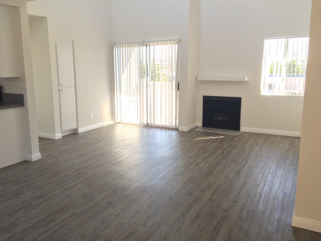 Jasne wnętrze po odnowieniu w Bytomiu: ściany pomalowane na biało, panele podłogowe imitujące drewno, białe drzwi balkonowe z pionowymi żaluzjami i kominek.