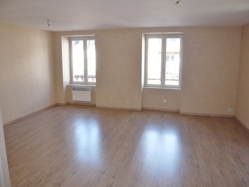 Pusty pokój po remoncie z drewnianą podłogą, świeżo pomalowanymi ścianami w odcieniach beżu, dwoma oknami z białymi ramami i grzejnikiem pod jednym z nich.