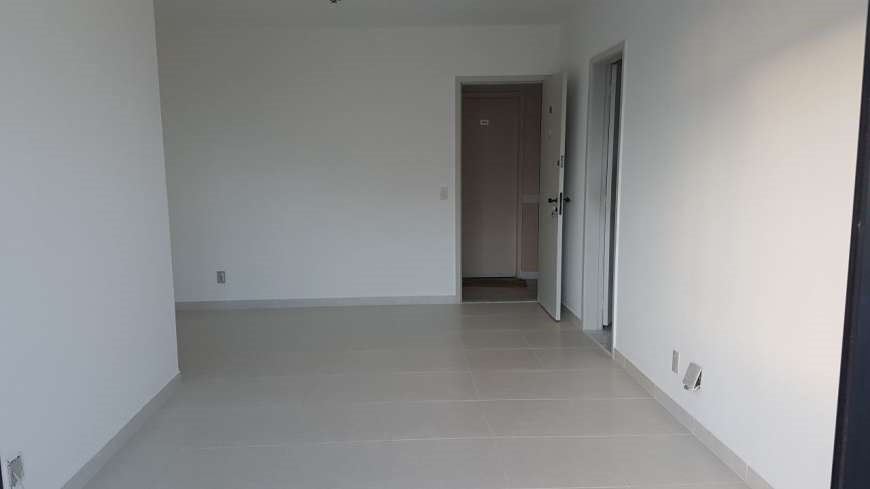 Puste, świeżo pomalowane na biało pomieszczenie z szarą podłogą z płytek, widoczne otwarte drzwi wewnętrzne i fragment ościeżnicy drzwi wejściowych.