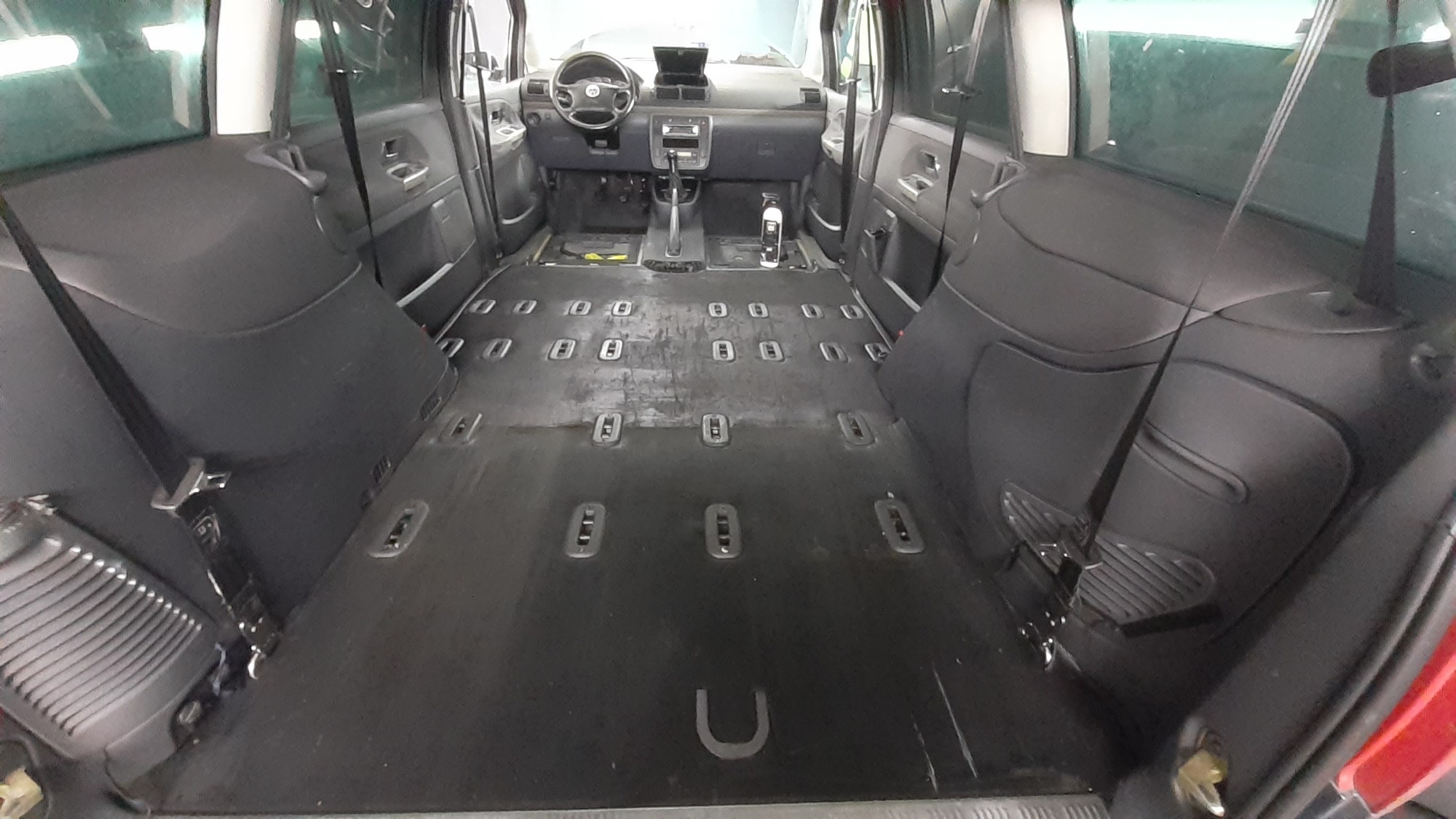 Wnętrze samochodu osobowego po demontażu siedzeń, przygotowane do czyszczenia tapicerki podłogowej, widoczny środek czyszczący na desce rozdzielczej.