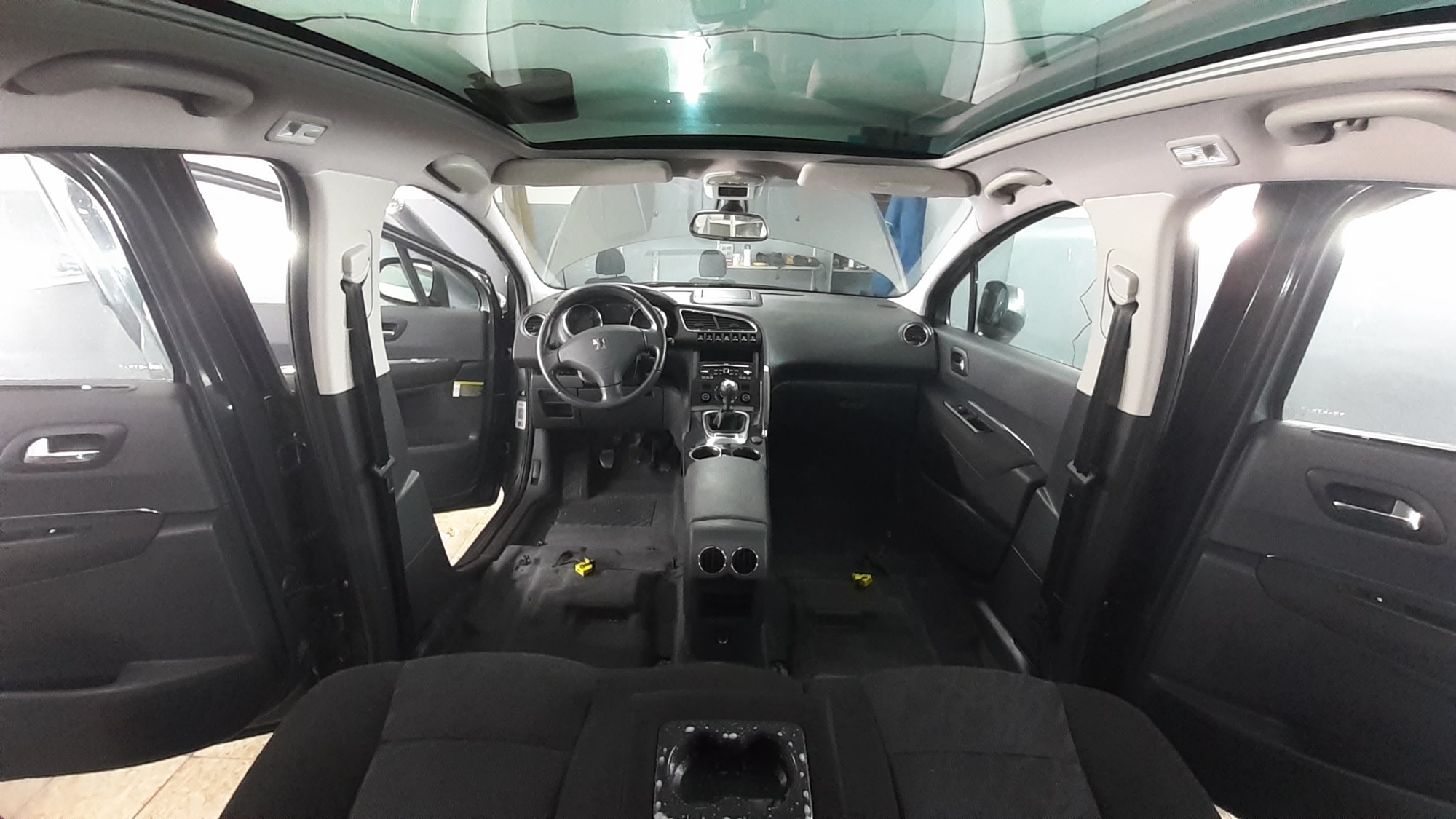 Wnętrze samochodu Peugeot 5008 z widocznymi śladami demontażu tapicerki przed praniem, z otwartymi drzwiami i widocznym dachem panoramicznym.