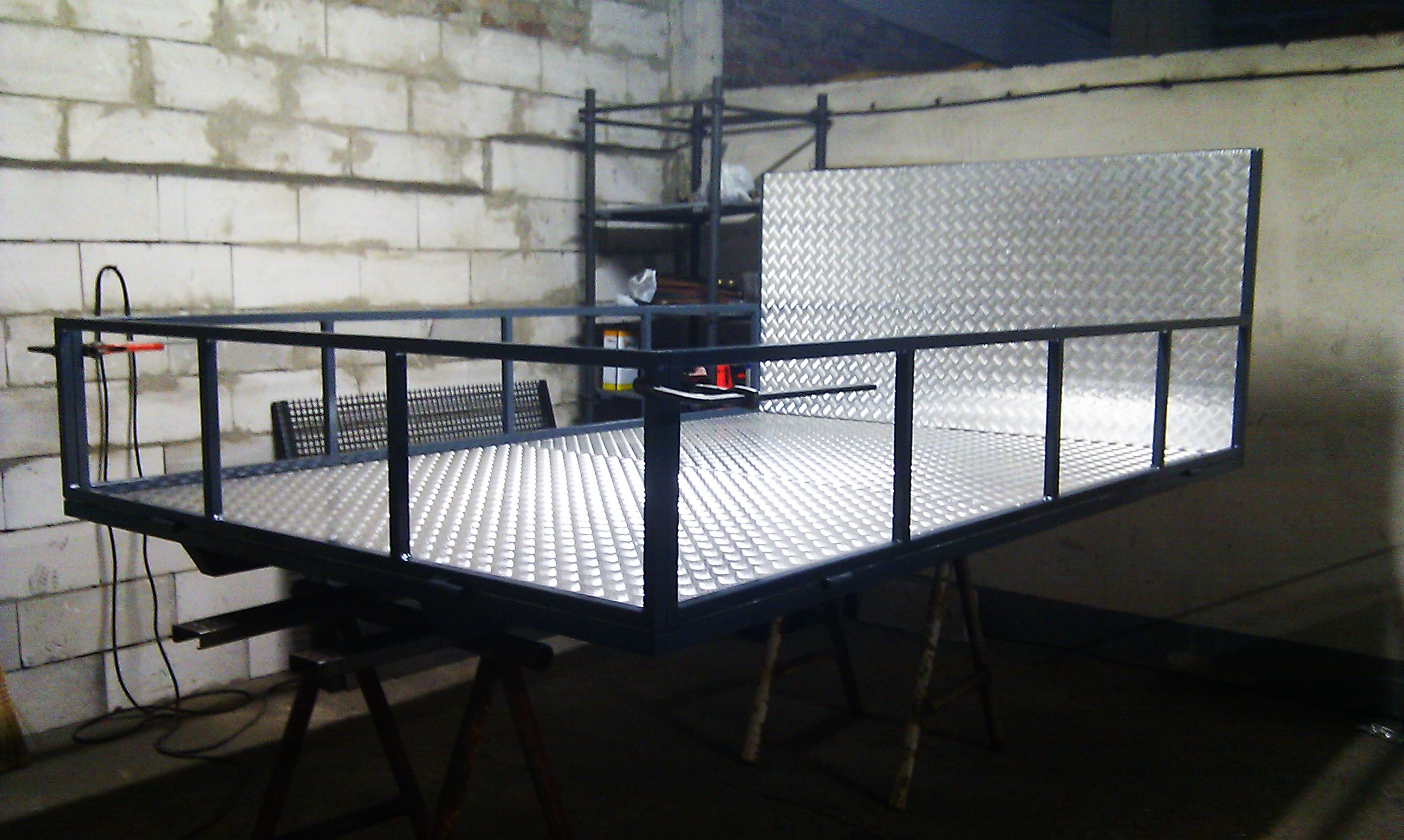 Konstrukcja ramy przyczepy z blachy ryflowanej, spawana z profili stalowych, ustawiona na kozłach w warsztacie.