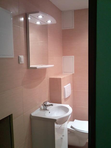 Ukończona łazienka w odcieniach beżu z narożną umywalką, toaletą i podświetlanym lustrem z półką.