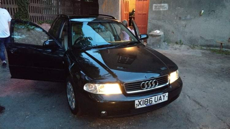 Czarny samochód kombi Audi A4 z otwartymi drzwiami, zaparkowany na zewnątrz budynku z szarą ścianą i czerwonymi drzwiami.