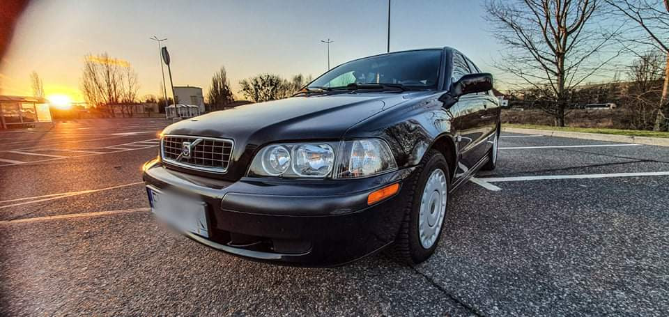 Czarny samochód Volvo S40 na parkingu o zachodzie słońca, widok z przodu, z widocznymi detalami karoserii i oponami zimowymi.