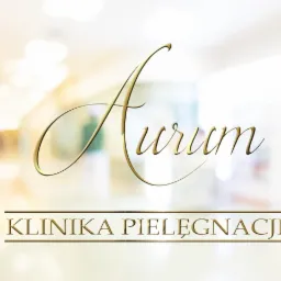 Złote logo 'Aurum Klinika Pielęgnacji' na szklanej powierzchni, z rozmytym wnętrzem kliniki w tle.