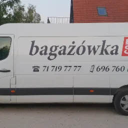 Biały samochód dostawczy z logo firmy bagażówka.com i numerami telefonów zaparkowany na żwirowej drodze przed domem.