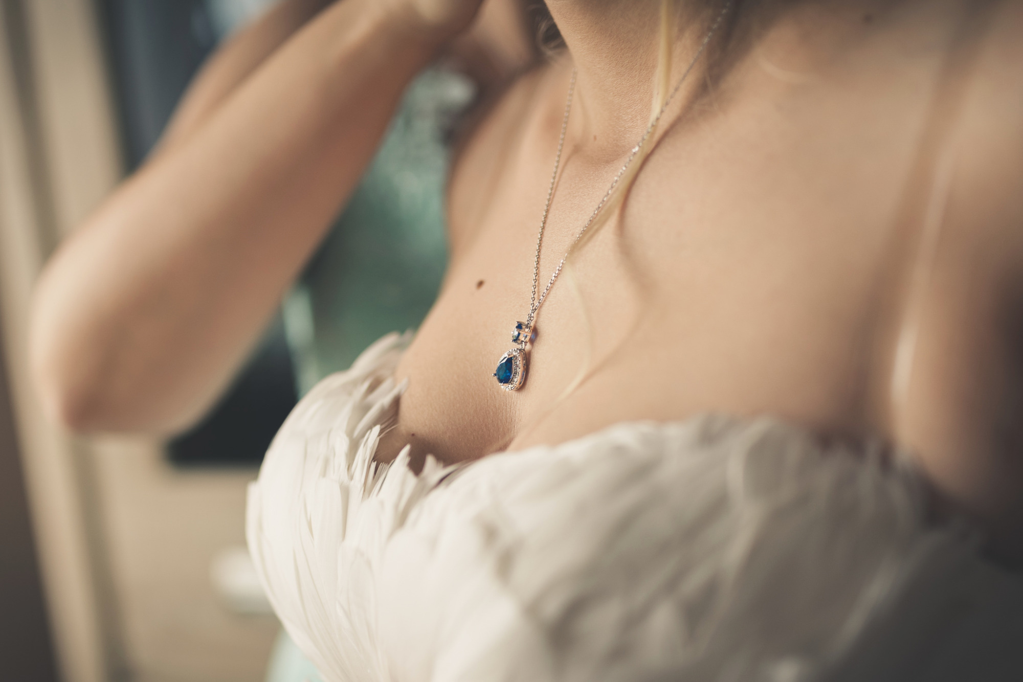 Panna młoda w białej sukni z piórami, z niebieskim naszyjnikiem w kształcie łzy, przygotowująca się do ceremonii.
