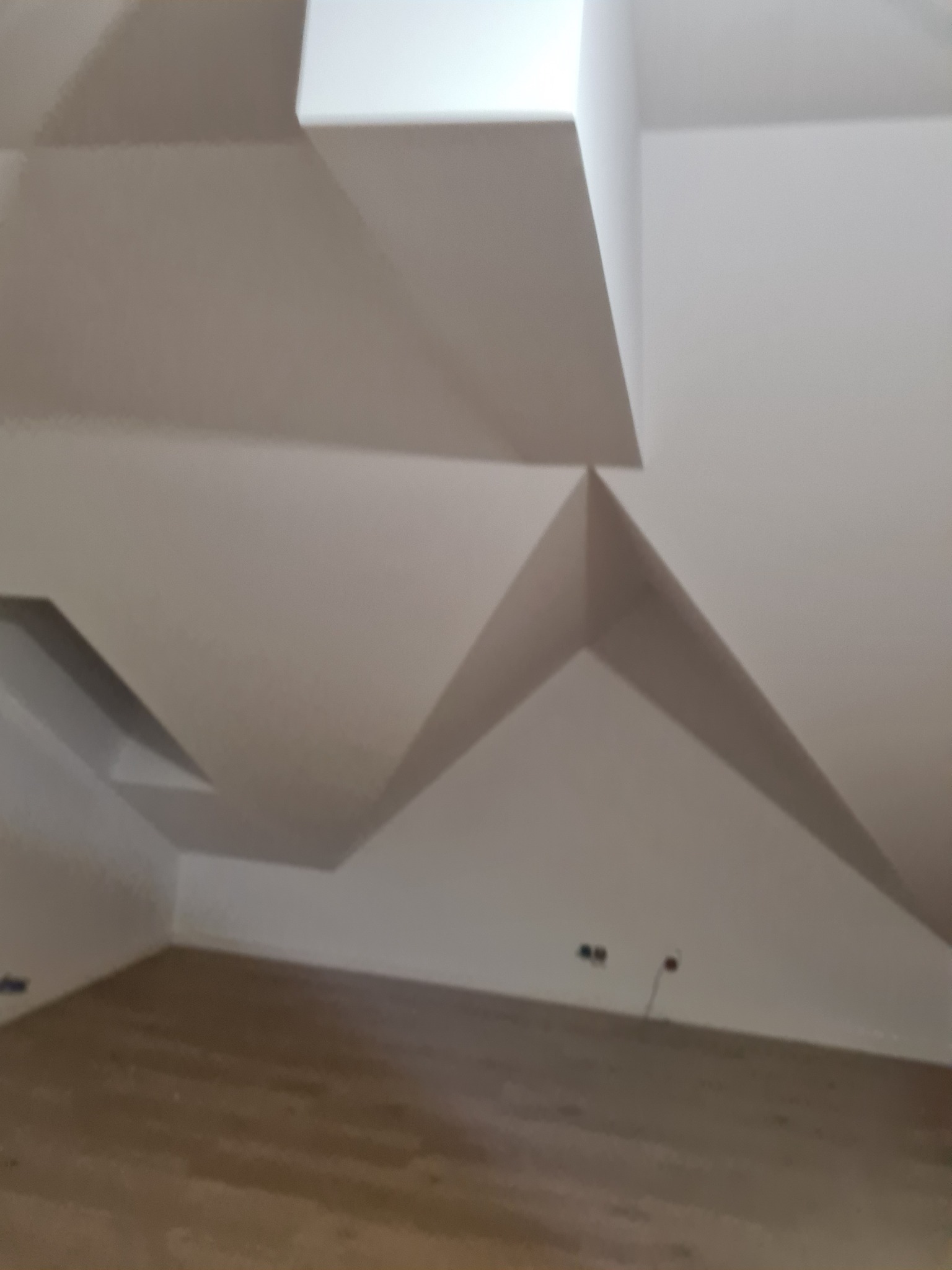 Wykończone poddasze w Lesznie z nietypową konstrukcją sufitu z płyt karton gips, widoczne wystające elementy i załamania tworzące geometryczny wzór.