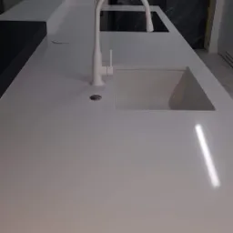 Biały, matowy blat kuchenny z wbudowanym zlewem i minimalistyczną, łukową baterią, widoczne zabezpieczenia folią malarską w tle.