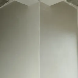 Świeżo wykończone ściany i sufit w narożniku pomieszczenia, widoczne ślady po szpachlowaniu i gładzi, surowy betonowy strop z widocznymi niedoskonałościami, w rogu oparta listwa przypodłogowa.