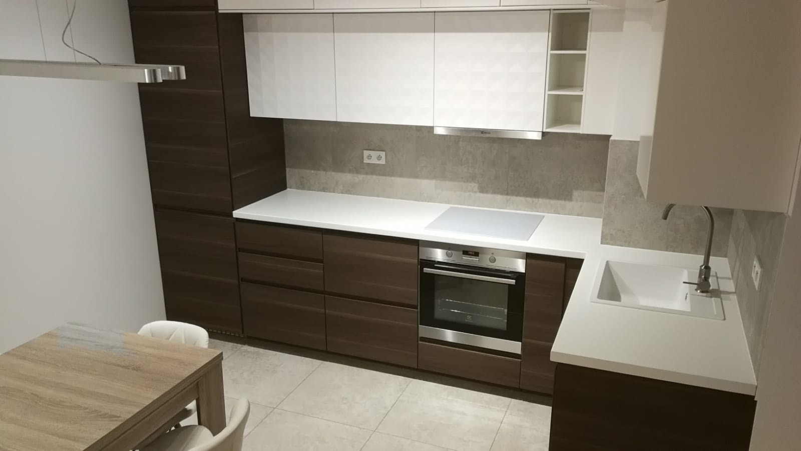 Nowoczesna kuchnia z ciemnymi, drewnopodobnymi szafkami dolnymi i białymi szafkami górnymi z geometrycznym wzorem, jasnym blatem, srebrnym piekarnikiem i płytą indukcyjną, widziana z perspektywy...