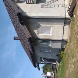 Dom z nowym, brązowym dachem z dachówki ceramicznej, świeżo zamontowane rynny w kolorze dachu, elewacja w trakcie wykańczania, okna zabezpieczone folią.