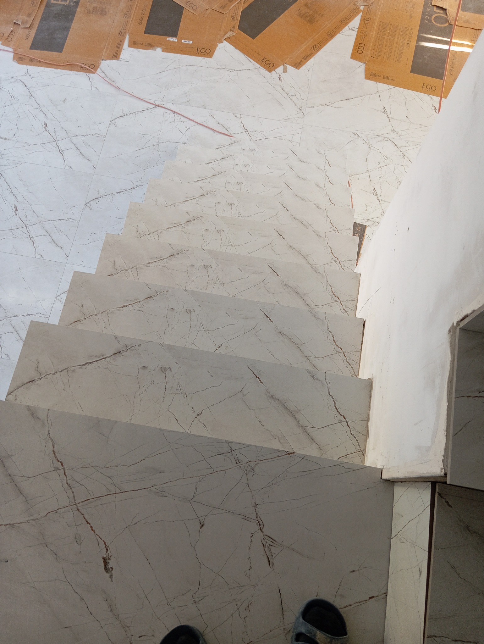 Wykończone schody w Bydgoszczy wyłożone płytkami imitującymi marmur, widok z góry na kafelki oraz kartony po płytkach. Na dole kadru widoczne stopy w klapkach.