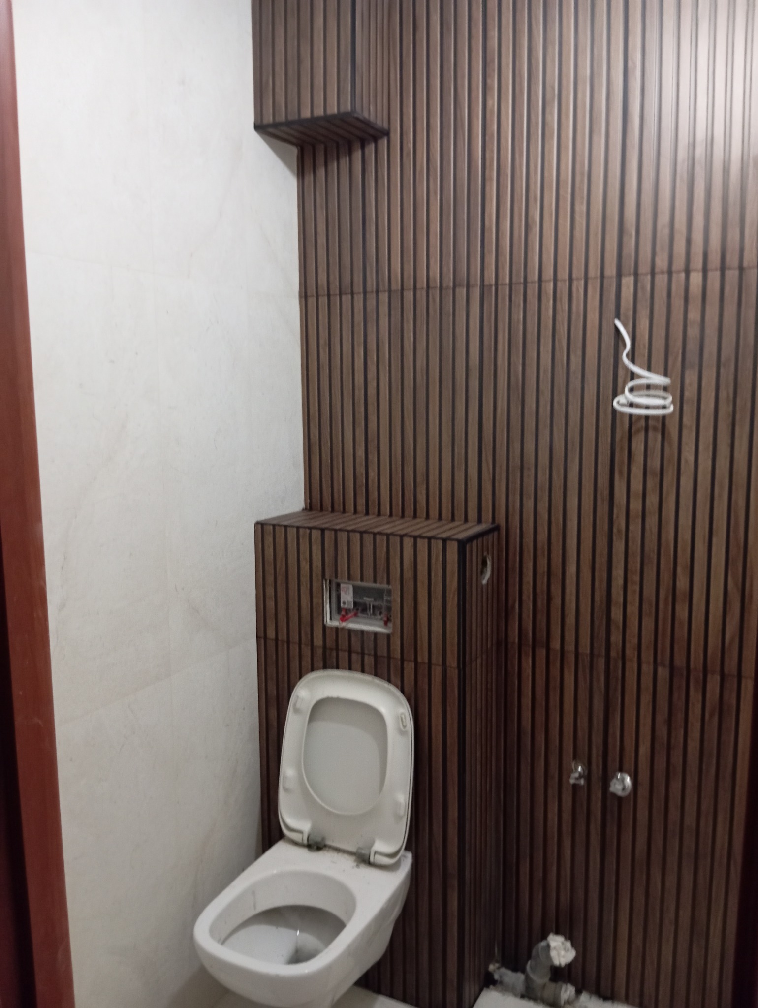 Nowoczesna toaleta z drewnopodobnymi panelami ściennymi i ukrytą spłuczką, prezentująca minimalistyczny design i funkcjonalność.