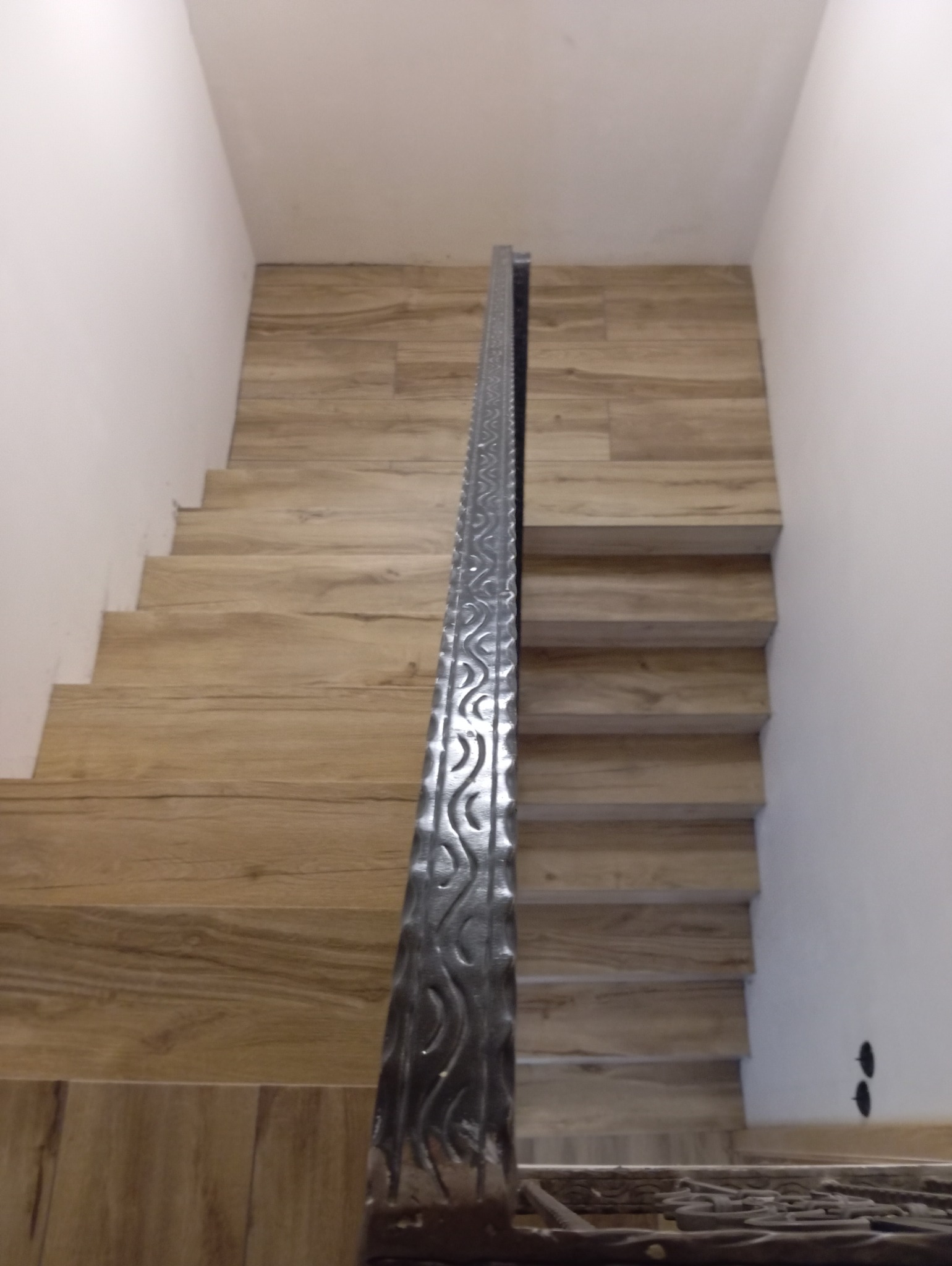 Schody wyłożone panelami imitującymi drewno z ozdobną, metalową balustradą, widok z dołu.