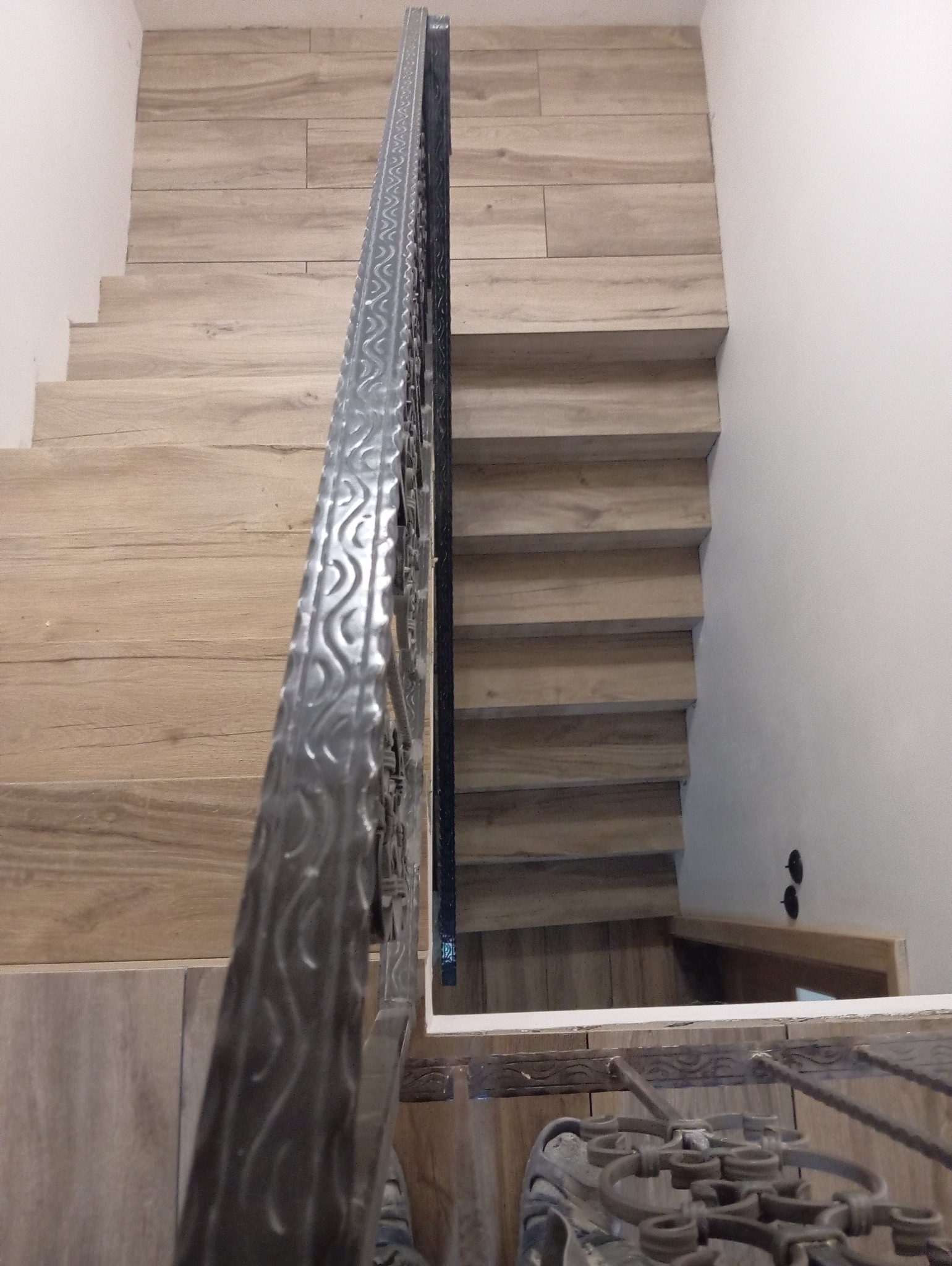 Schody wyłożone płytkami imitującymi drewno, z metalową balustradą o zdobnym wzorze, widok z góry.