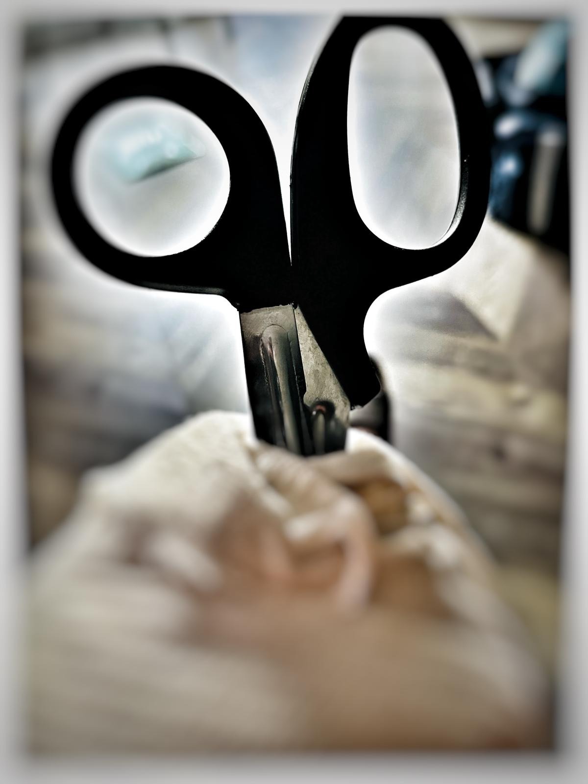 Czarne nożyczki z metalowym ostrzem przecinają bandaż, widoczne z bliska pod kątem.