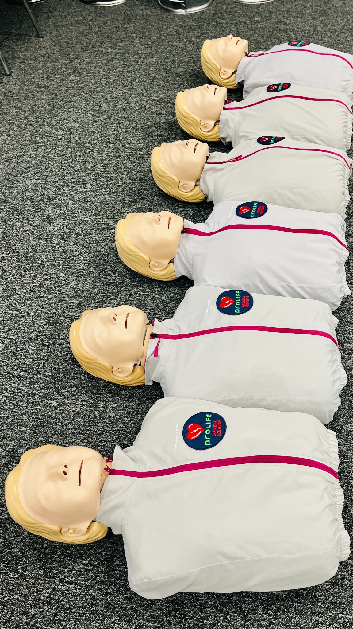 Manekiny do ćwiczeń resuscytacji krążeniowo-oddechowej ułożone rzędem na podłodze we Wrocławiu, widoczne logo ProLife Szkolenia Medyczne na każdym manekinie.