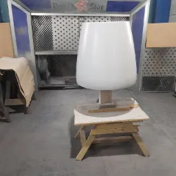 Biały, lakierowany element meblowy w lakierni w Ostrowie Wielkopolskim, przygotowany do dalszej obróbki, na tle kabiny lakierniczej.