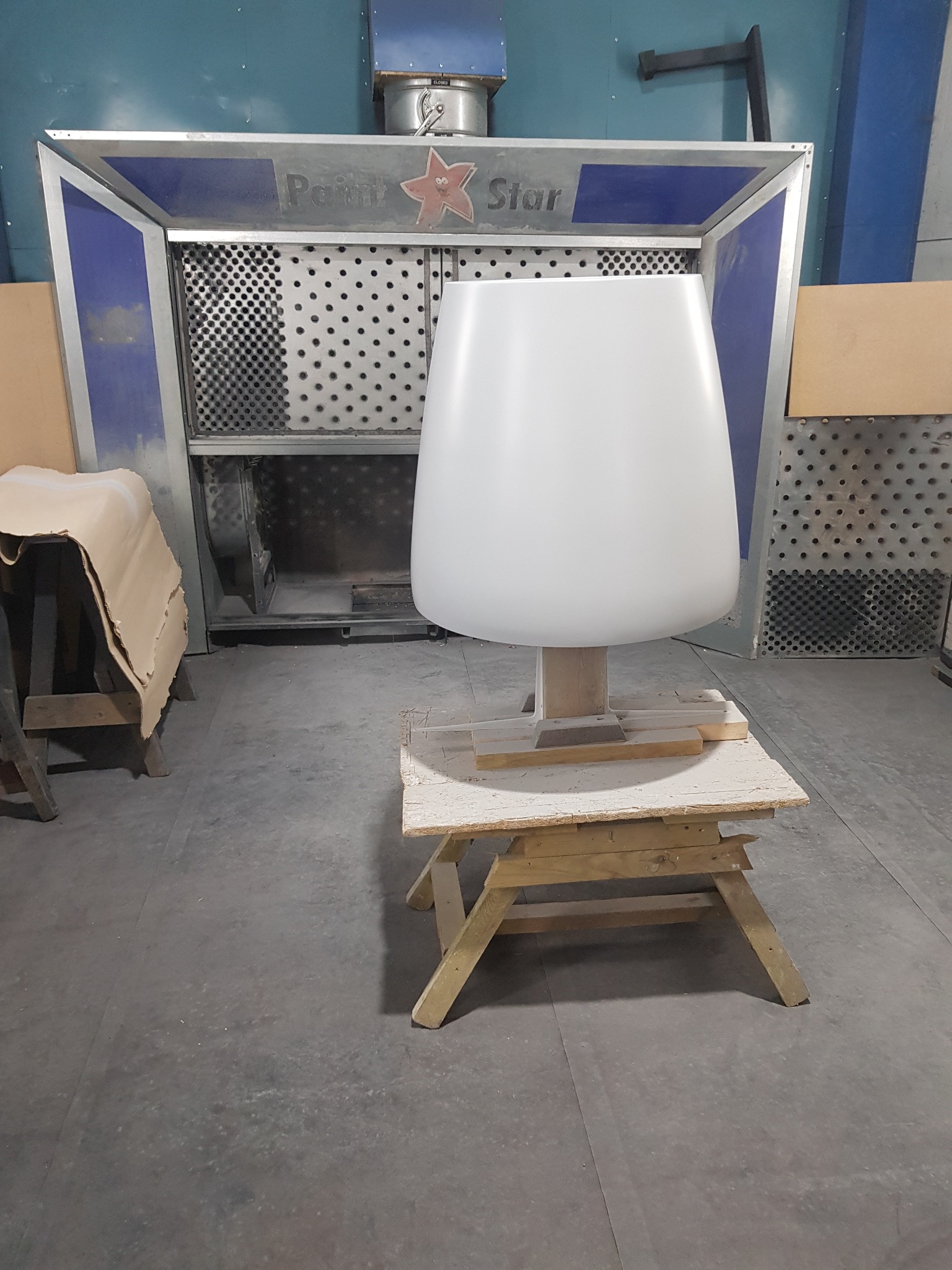 Biały, lakierowany element meblowy w lakierni w Ostrowie Wielkopolskim, przygotowany do dalszej obróbki, na tle kabiny lakierniczej.