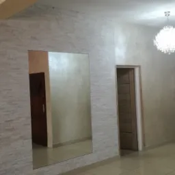 Korytarz z dekoracyjną ścianą z białych płytek imitujących kamień, duże lustro wbudowane w ścianę, ściany pomalowane na jasny beż, kryształowy żyrandol