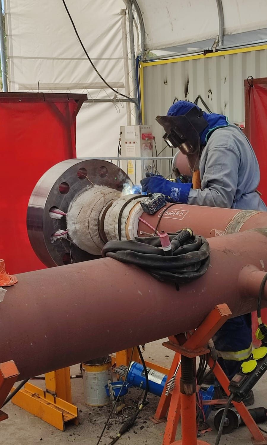 Spawanie rurociągu z kołnierzem w osłoniętym stanowisku pracy, widoczne zabezpieczenia termiczne i iskry spawania.