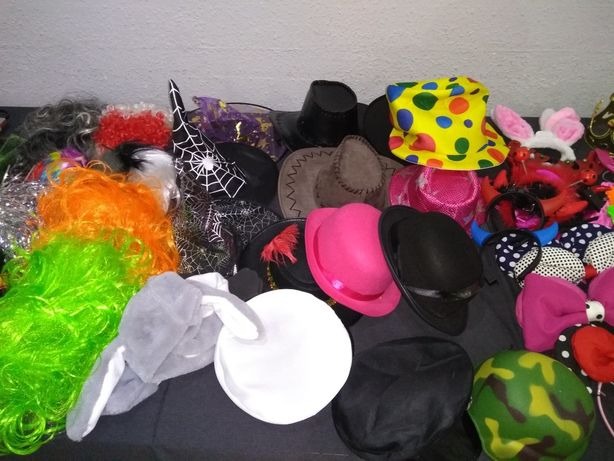 Zbiór różnorodnych rekwizytów: kolorowe peruki, kapelusze w kropki, czapki wiedźmy z pajęczyną, uszy królika i inne akcesoria do sesji zdjęciowych.