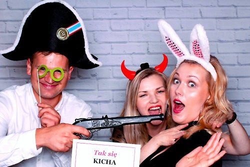 Trzy osoby pozujące w przebraniach z rekwizytami przed ceglaną ścianą: mężczyzna z zielonymi okularami na patyku i kapeluszem pirata, kobieta z rogami diabła i kobieta z uszami królika