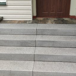 GAL-Bruk - Nowe, betonowe schody wejściowe z czterema stopniami i boczną ścianką z bloków betonowych, prowadzące do brązowych drzwi wejściowych, z widocznym fragmentem elewacji z sidingu.