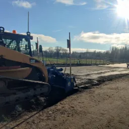 Żółta ładowarka gąsienicowa CAT 287B z frezarką do asfaltu przygotowuje podłoże pod budowę, widoczne ślady gąsienic i świeżo sfrezowany teren.