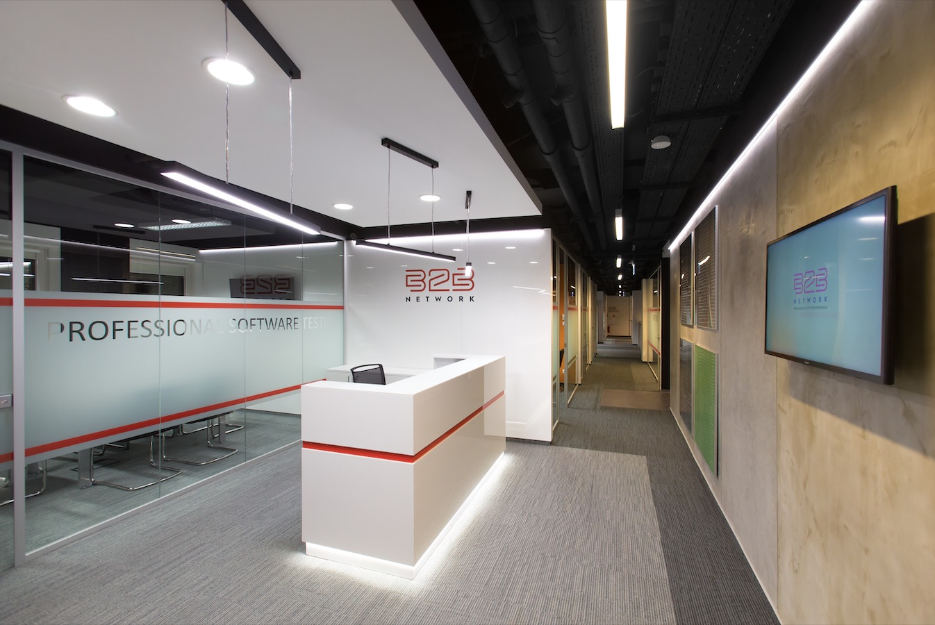 Nowoczesne biuro firmy IT z recepcją, szklaną salą konferencyjną z napisem 'PROFESSIONAL SOFTWARE TESTING' i długim korytarzem z ekranem wyświetlającym logo 'B2B NETWORK'.