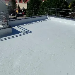 Wykończony, jasnoszary taras z metalową barierką, widok z góry na tle zabudowy miejskiej.