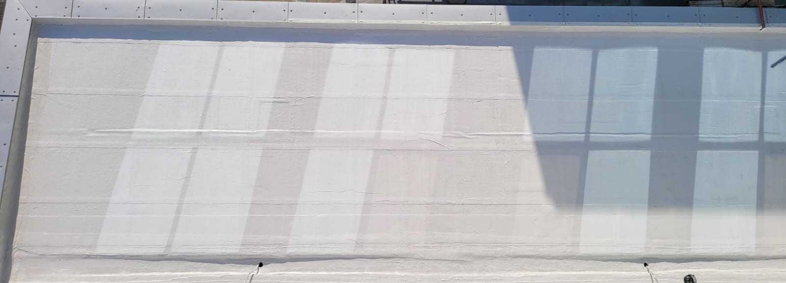 Biała, pozioma powierzchnia po hydroizolacji, z widocznymi śladami łączeń i cieniem, oświetlona naturalnym światłem.