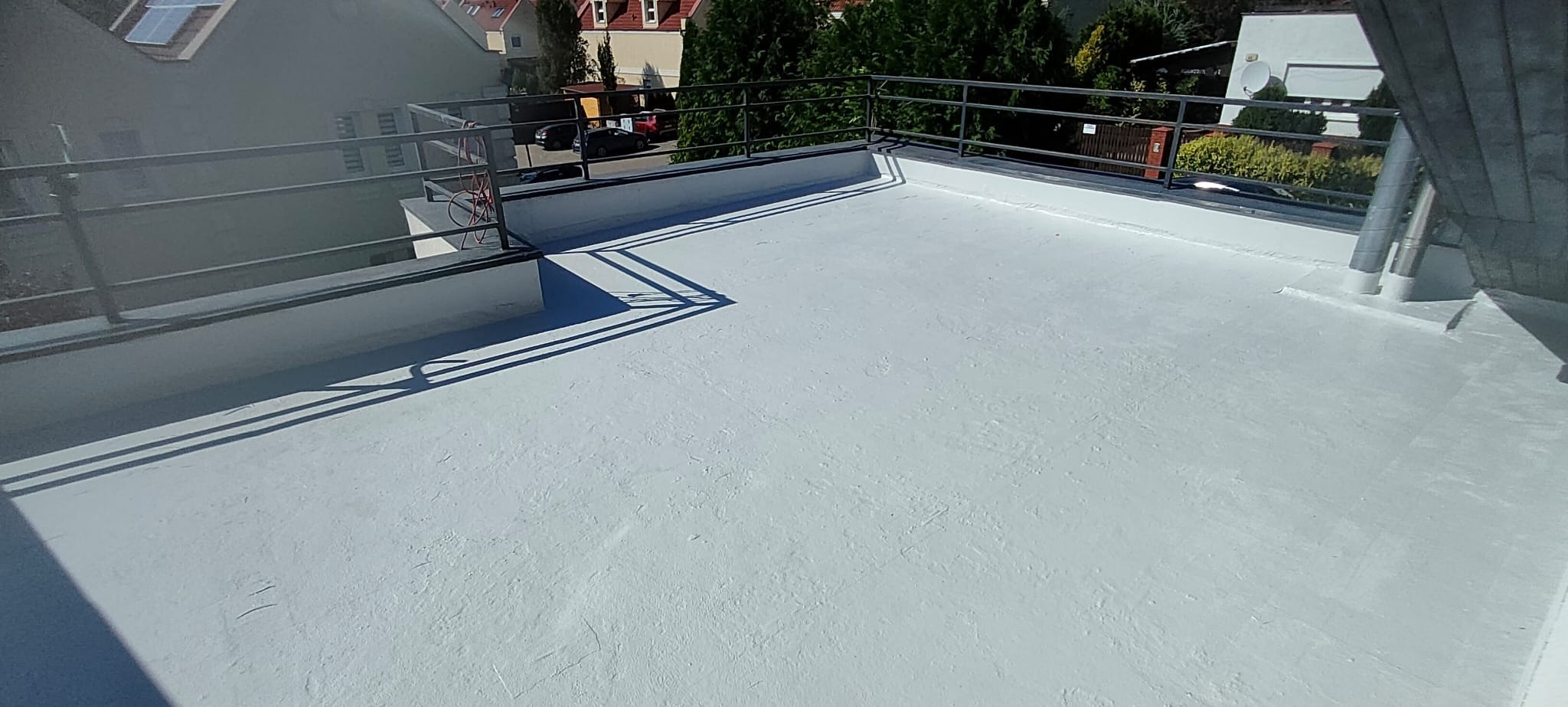 Wykończony, jasnoszary taras z metalową barierką, widok z góry na tle zabudowy miejskiej.