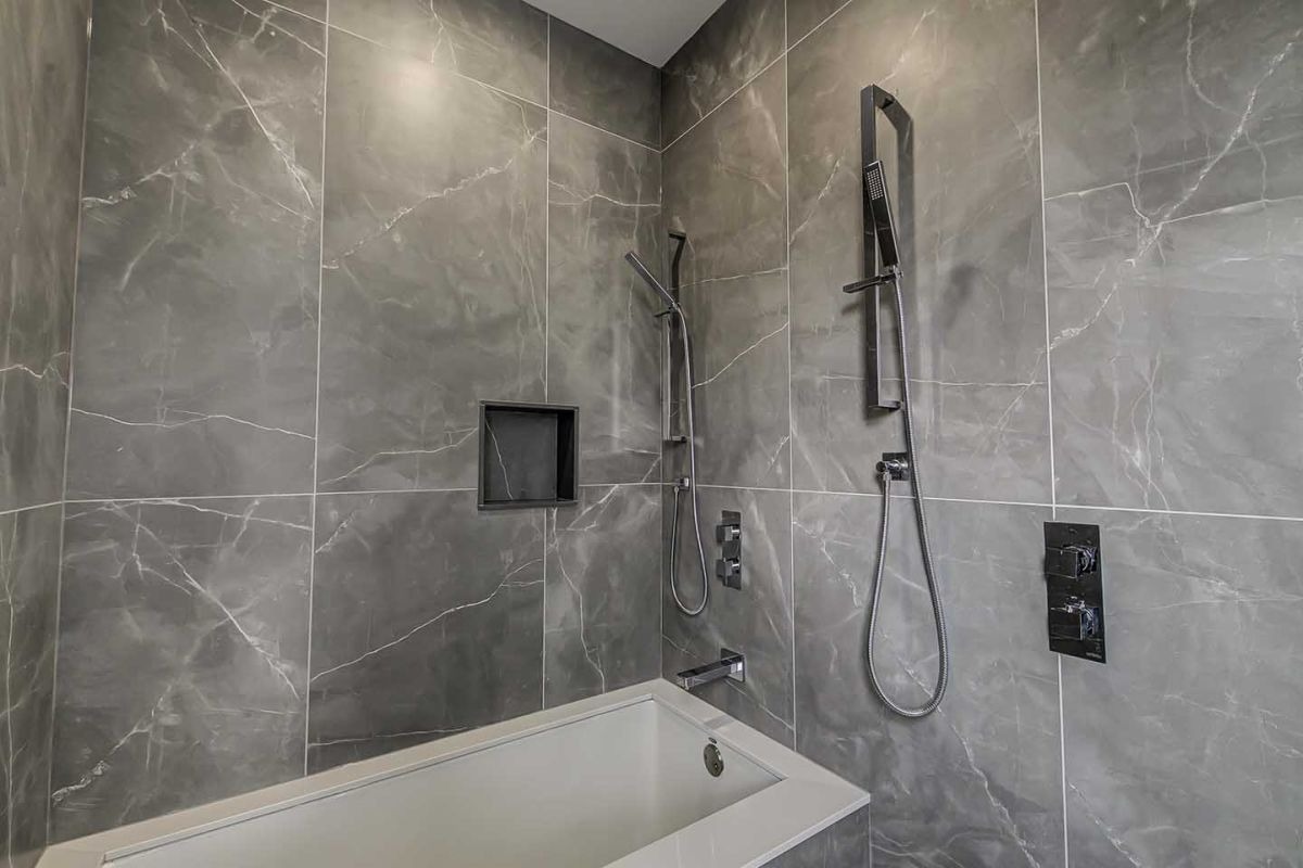 Nowoczesna łazienka z szarymi płytkami imitującymi marmur, wyposażona w designerską armaturę w kolorze czarnym i wnękę w ścianie.