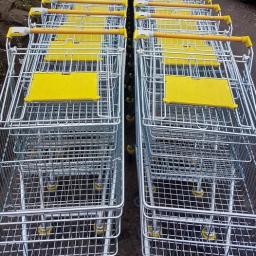 OSTEL Zbigniew Małyszka, Kamil Małyszka, Tomasz Małyszka s.c. - Rząd metalowych wózków sklepowych z żółtymi elementami, ustawionych jeden za drugim na zewnątrz.