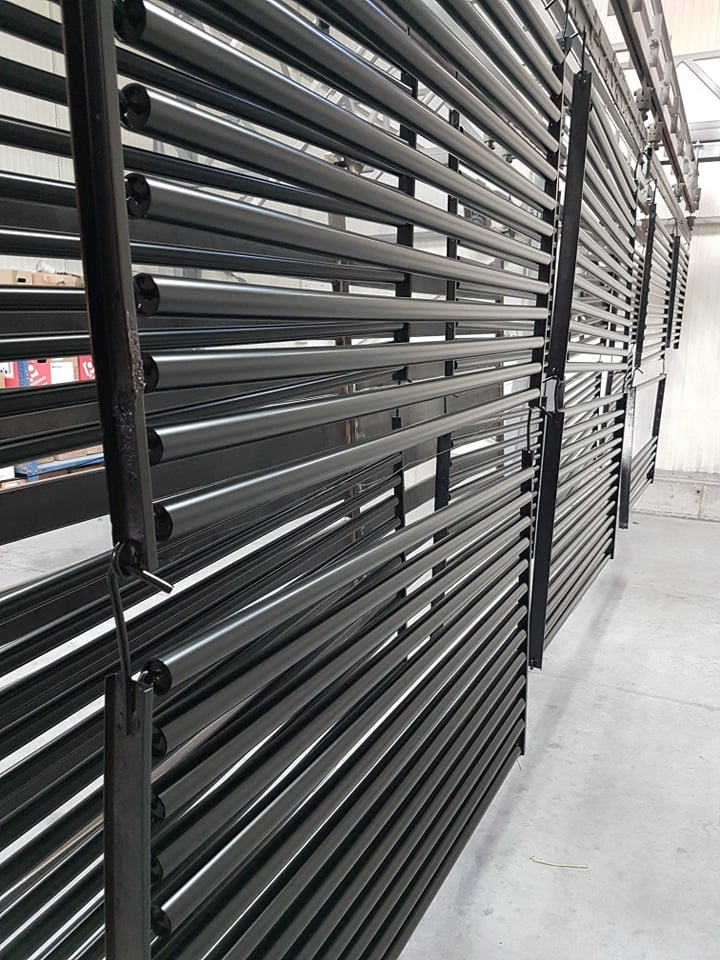 Czarne, metalowe rury po obróbce, zawieszone na wieszakach w hali produkcyjnej w Grochowie Szlacheckim, gotowe do dalszej obróbki lub transportu.