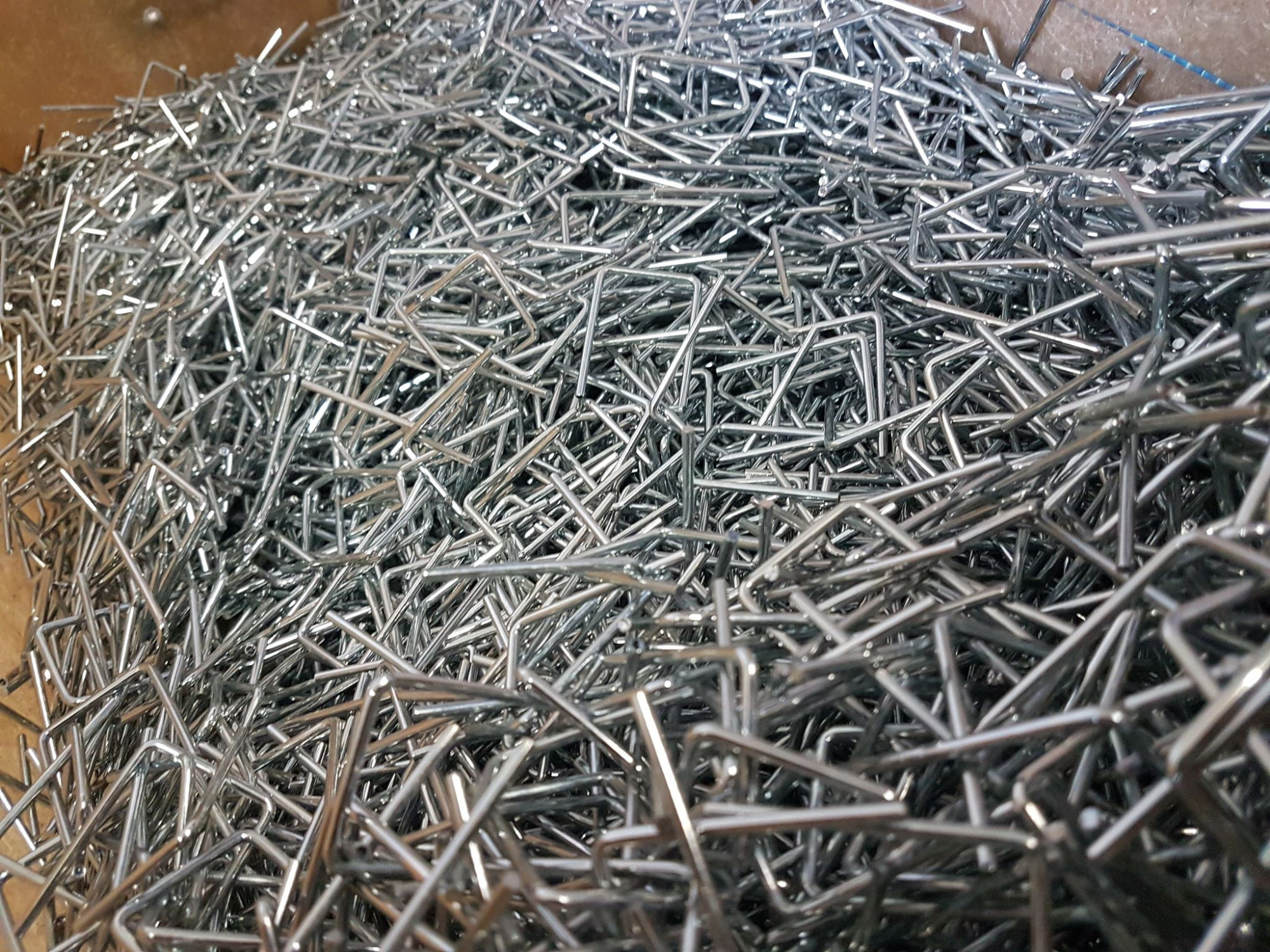Stalowe, ocynkowane pręty zagięte pod kątem prostym, ułożone chaotycznie w pojemniku, widoczne ślady obróbki.