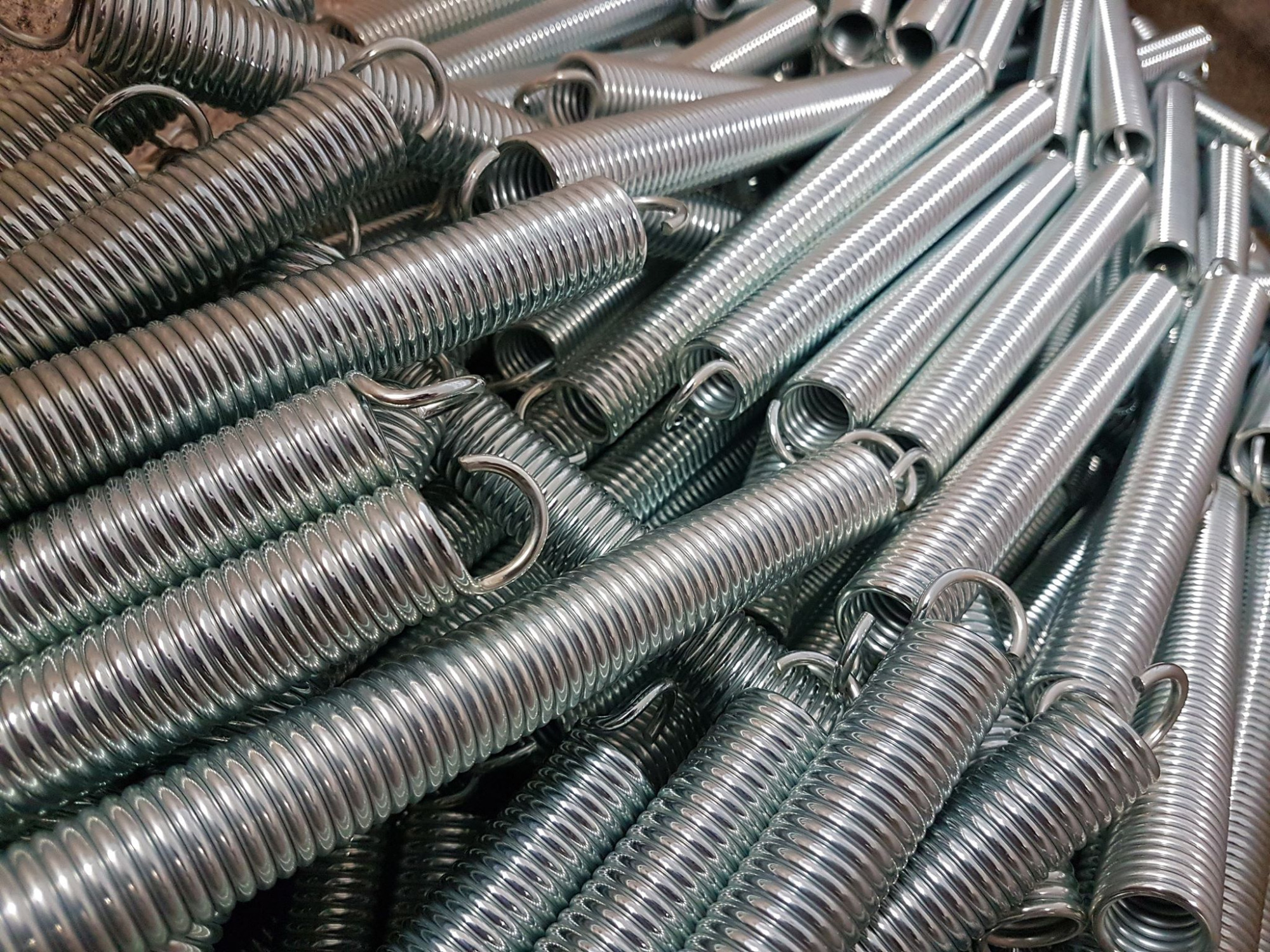 Stos srebrnych, metalowych sprężyn śrubowych z haczykami, ułożonych gęsto obok siebie, widoczny detaliczny wzór żłobień.
