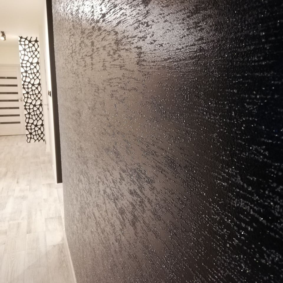 Ciemna ściana z dekoracyjną fakturą, widoczna w perspektywie, z fragmentem przedpokoju w tle i designerską ścianką działową.