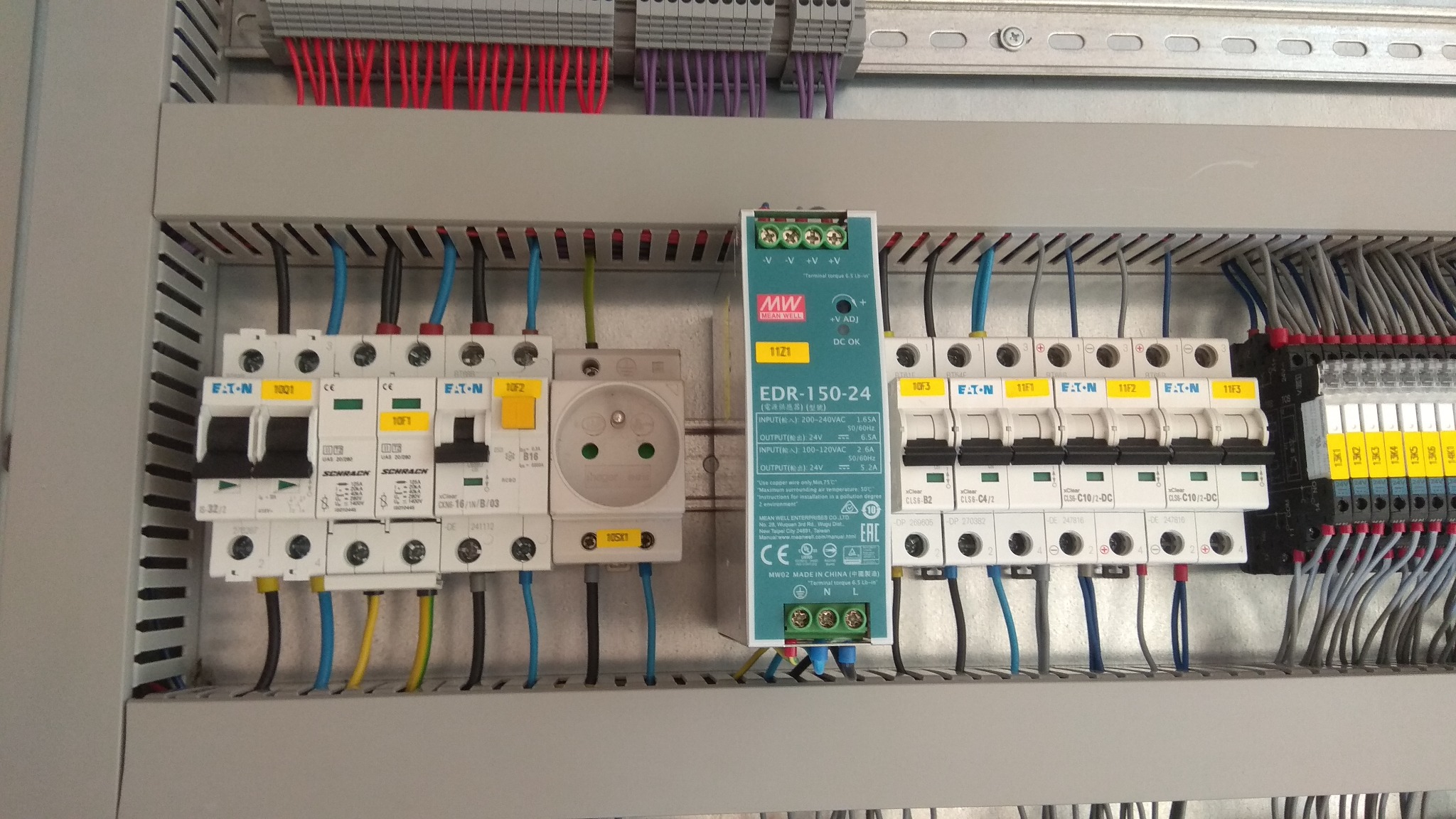 Wnętrze szafy sterowniczej z modułami Eaton, zasilaczem Mean Well EDR-150-24 i gniazdem, widoczne okablowanie i bezpieczniki.
