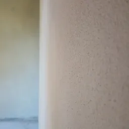 Beżowa, chropowata ściana po nałożeniu tynku maszynowego, widoczny fragment podłogi z przewodami w tle.