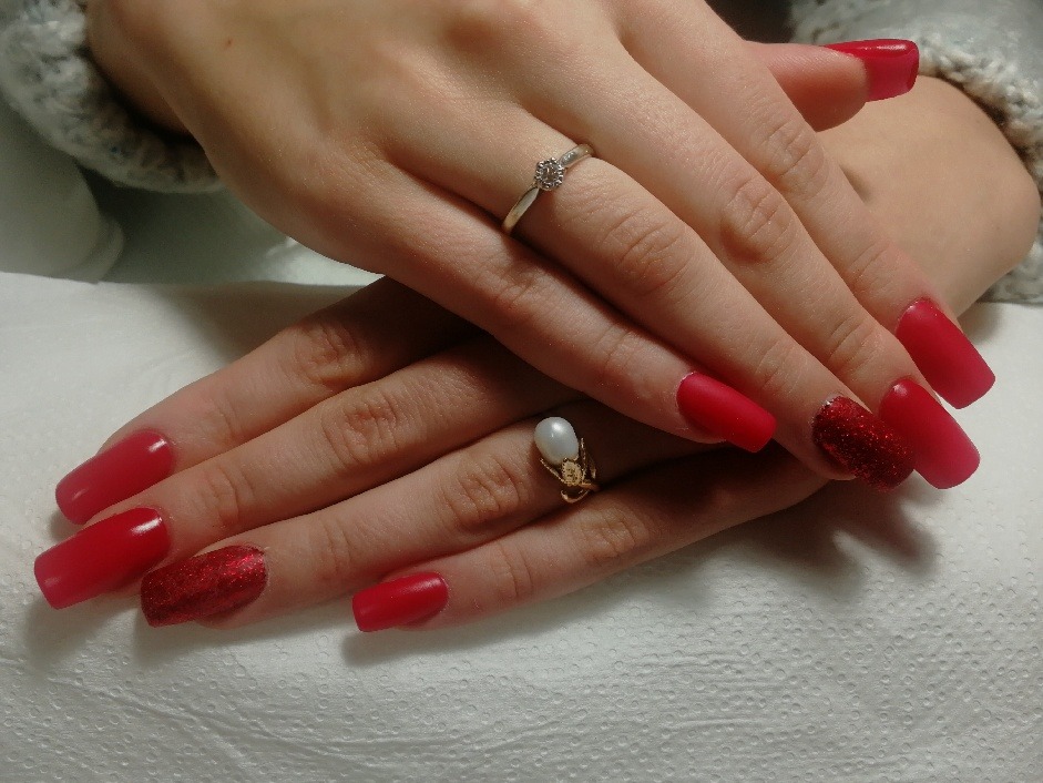 Dłonie z czerwonym manicure, jeden paznokieć z brokatem, pierścionek z perłą i pierścionek z diamentem na białym tle.