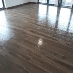 Połyskująca podłoga z płytek imitujących drewno ułożona w jodełkę, widoczne odbicie okien w gładkiej powierzchni.