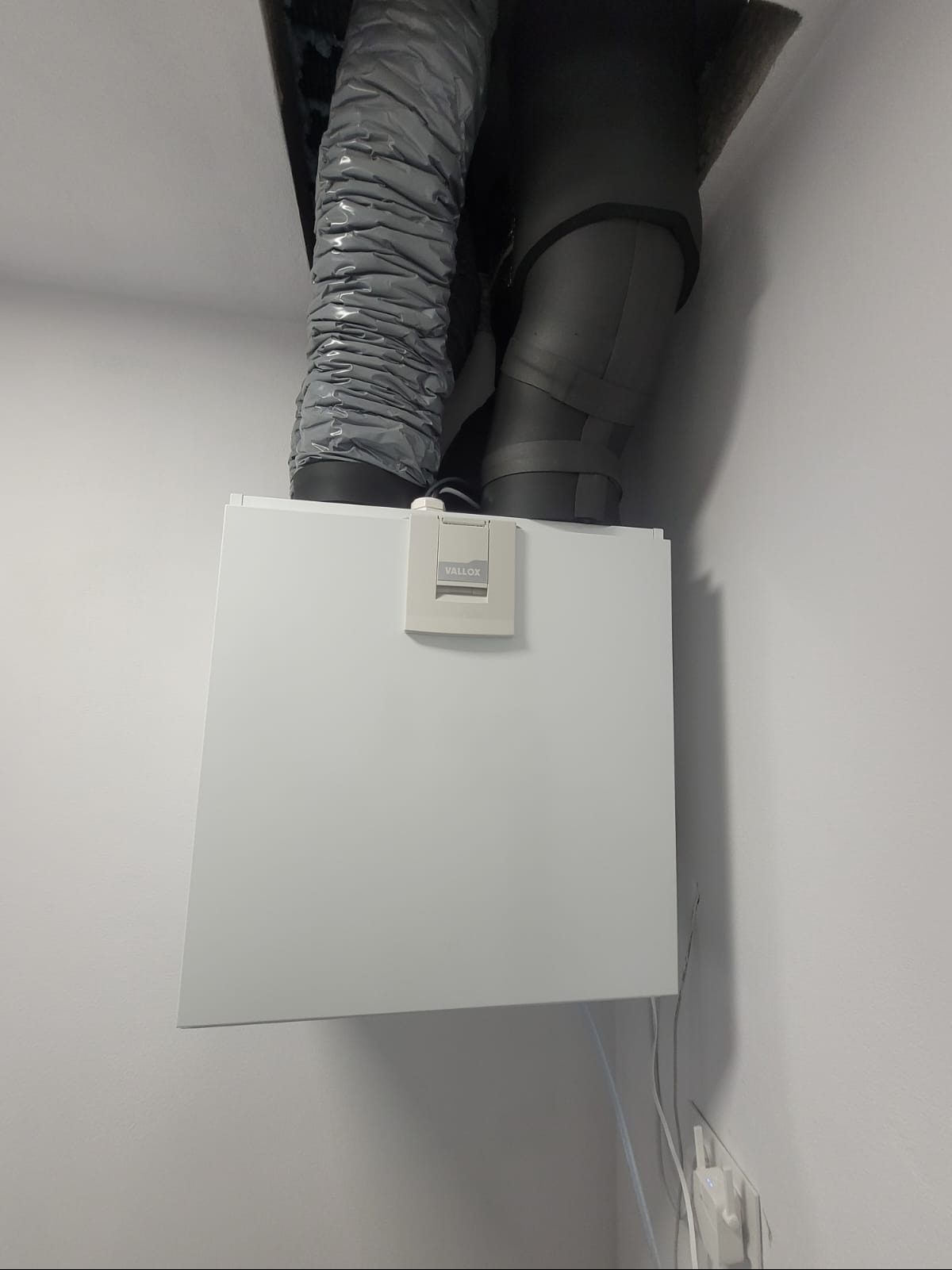 Zamontowany rekuperator Vallox 110MV Metalpic z podłączonymi przewodami wentylacyjnymi, widoczne przewody elektryczne przy ścianie.